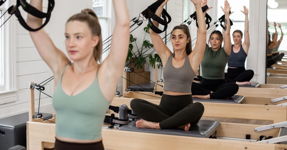 A group reformer class training together in a bright studio